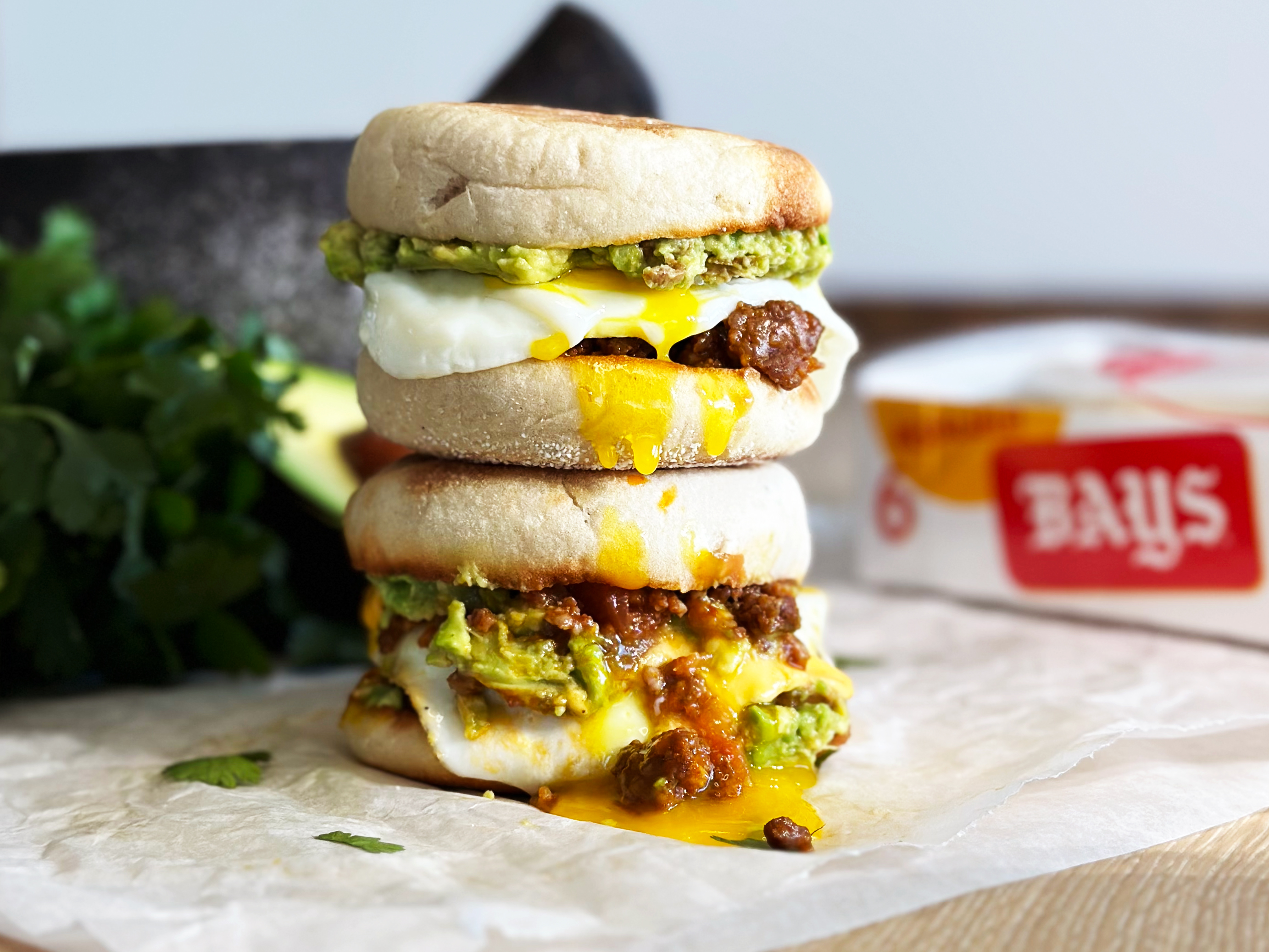 TWO SANDWICHES STACKED ON TOP OF EACHOTHER FILLED WITH SAUSAGE EGG AND AVOCADO SPREAD