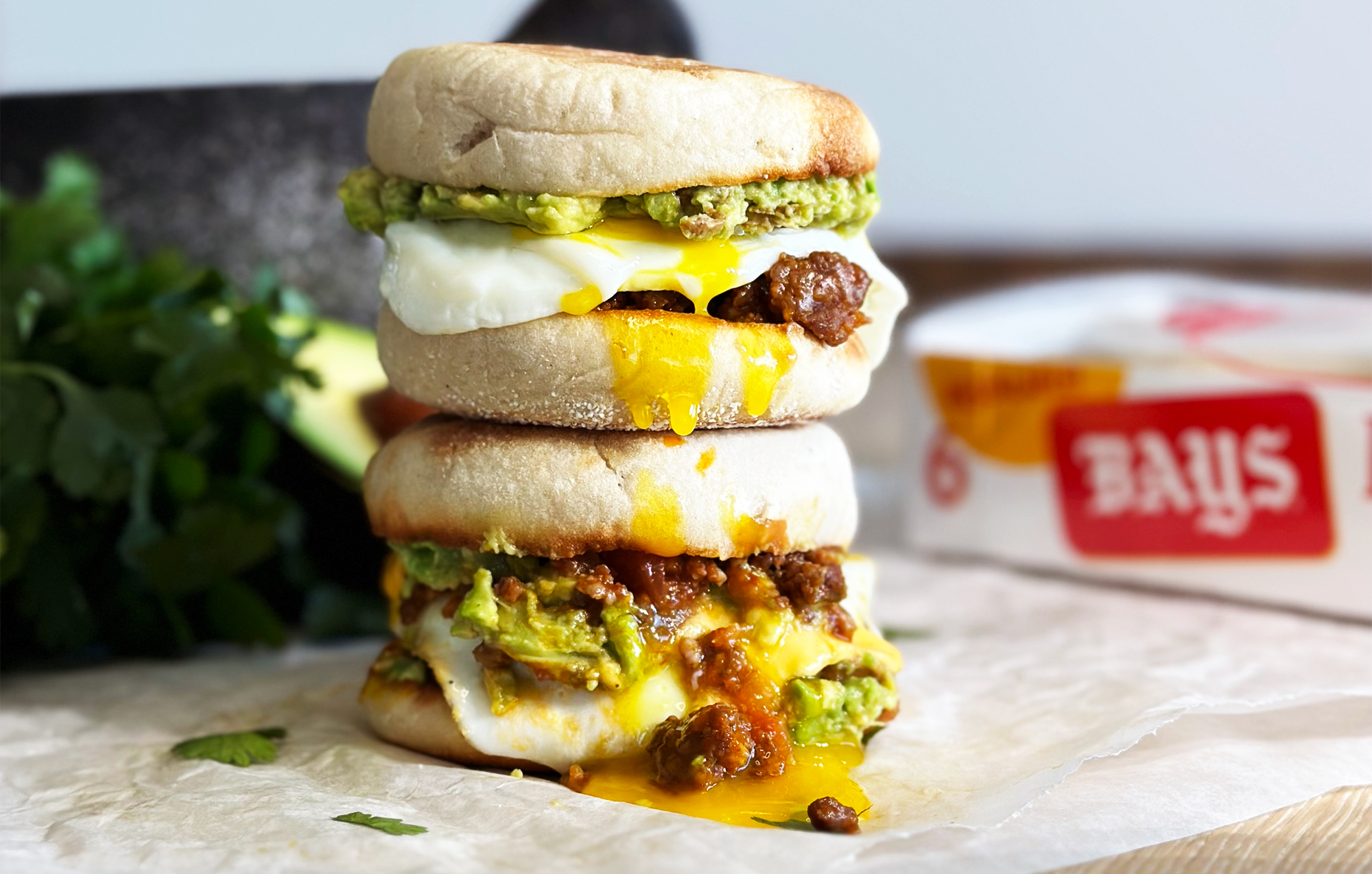 TWO SANDWICHES STACKED ON TOP OF EACHOTHER FILLED WITH SAUSAGE EGG AND AVOCADO SPREAD