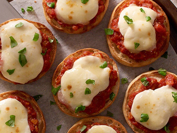 A TRAY OF ENGLISH MUFFINS WITH MELTED CHEESE ON TOMATO SAUCE