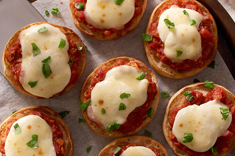 A TRAY OF ENGLISH MUFFINS WITH MELTED CHEESE ON TOMATO SAUCE