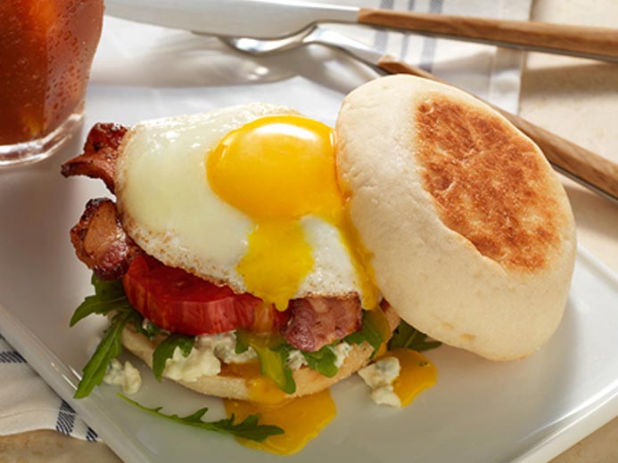 sunny side up egg on top of meat, veggies, and Bays English Muffins